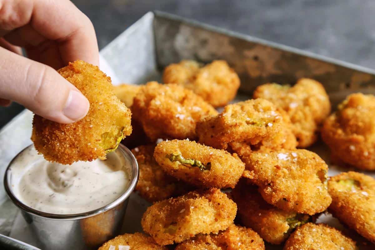 a hand dipping a fried pickle slice into ranch dip