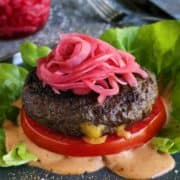 A stuffed burger on a lettuce wrap with pickled onions