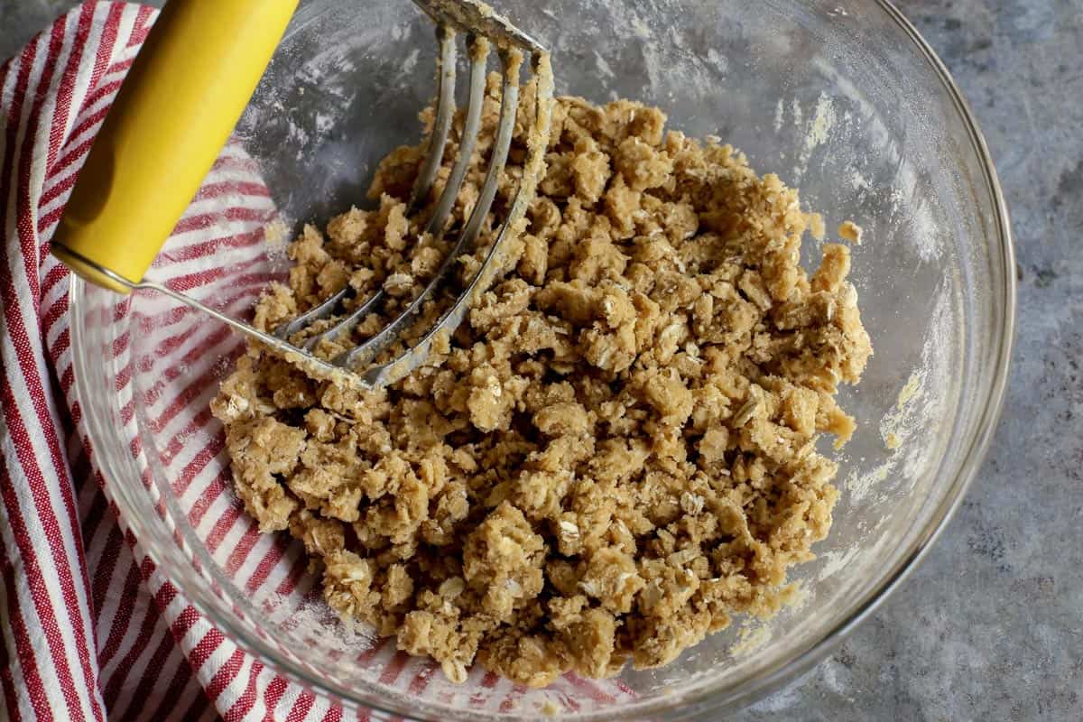 A glass bowl of apple crisp topping with a pastry blender