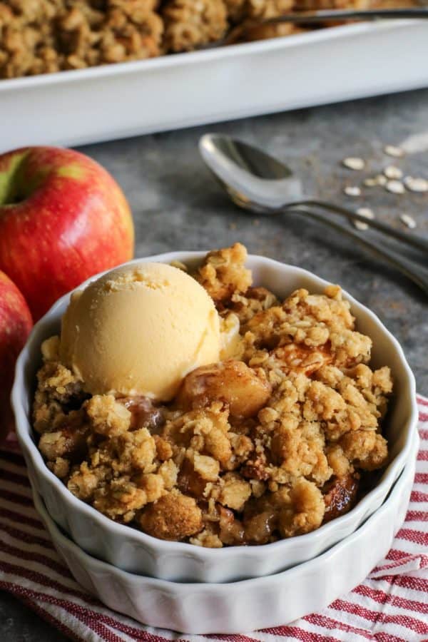 homemade apple crisp in a white dish with a scoop of vanilla ice cream