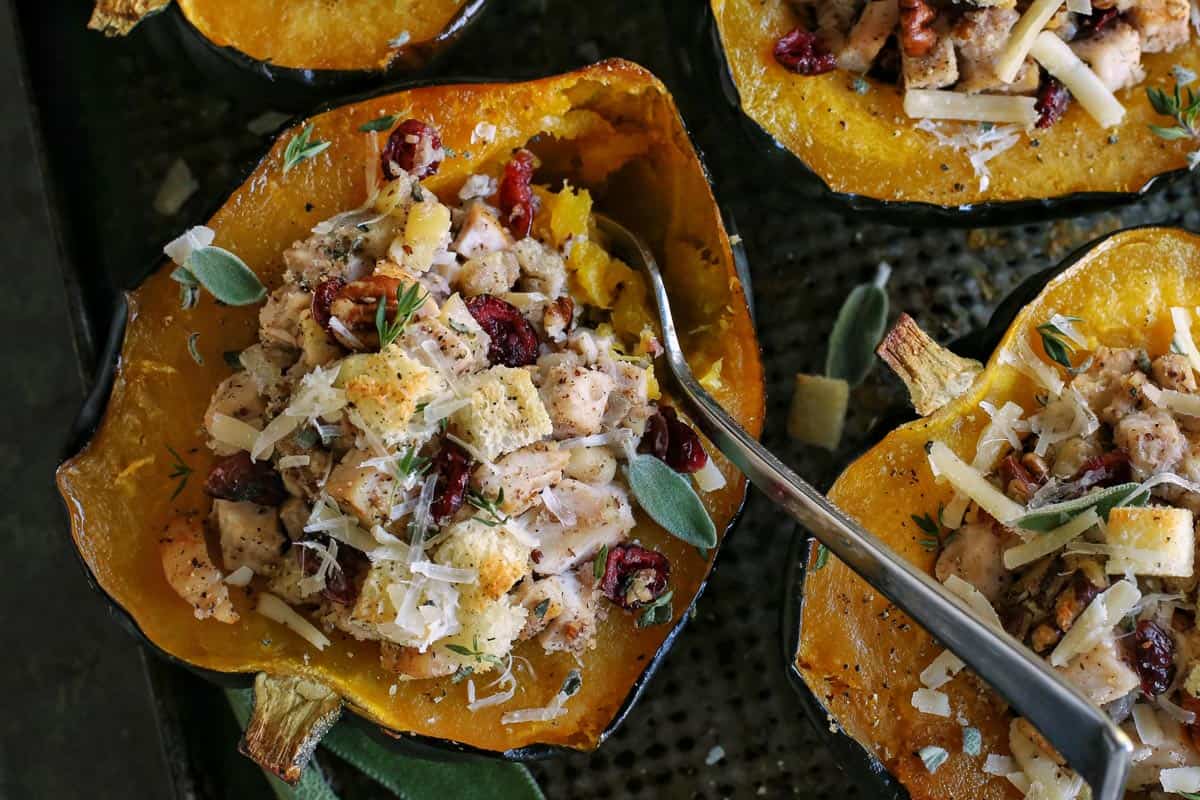a fork in a halved acorn squash that is stuffed with a turkey and dressing mixture