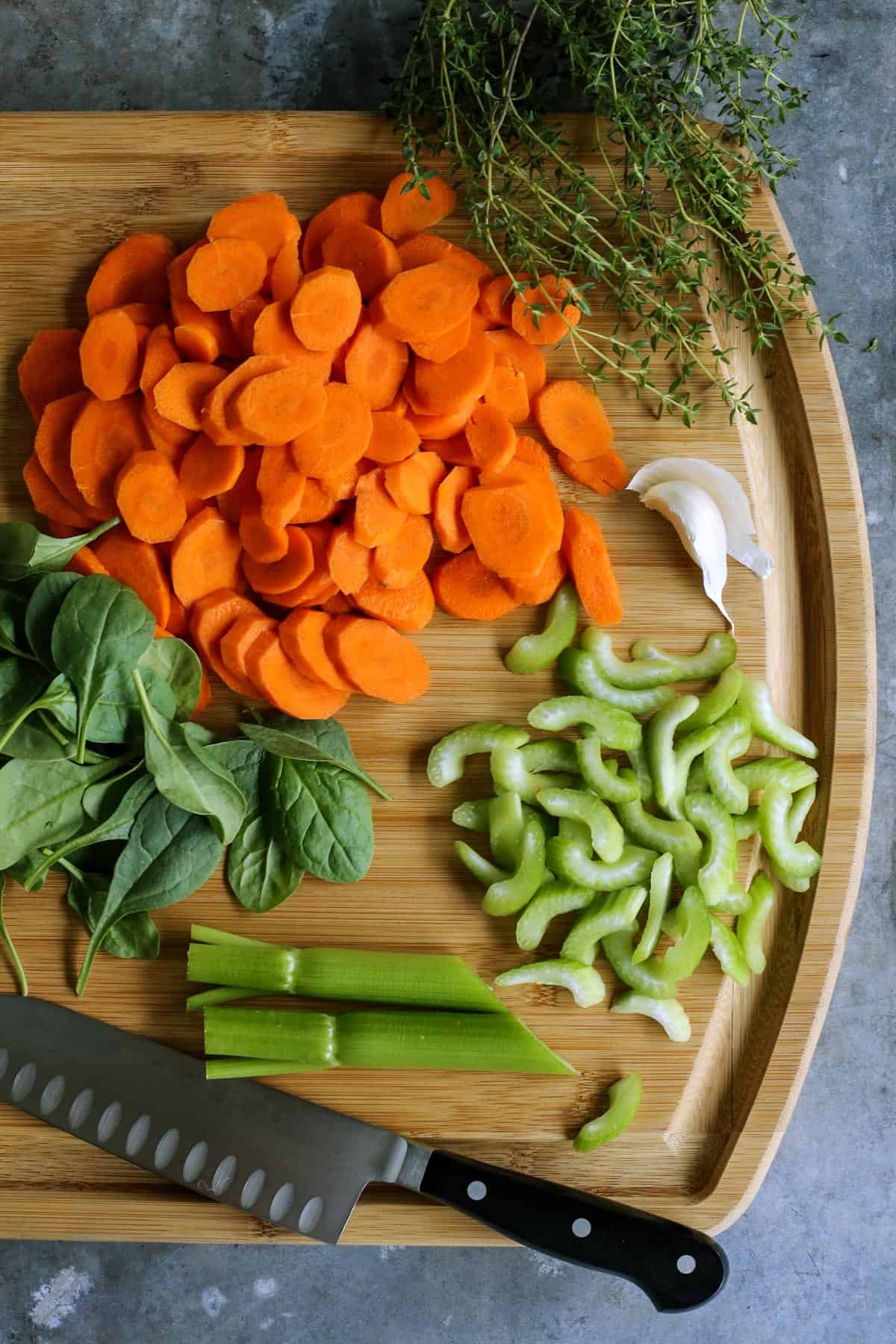 fresh carrots, celery, garlic, spinach, and thyme on cutting board with chef's knife