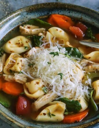 turkey tortellini soup in blue pottery bowl, with fresh Parmesan and herbs