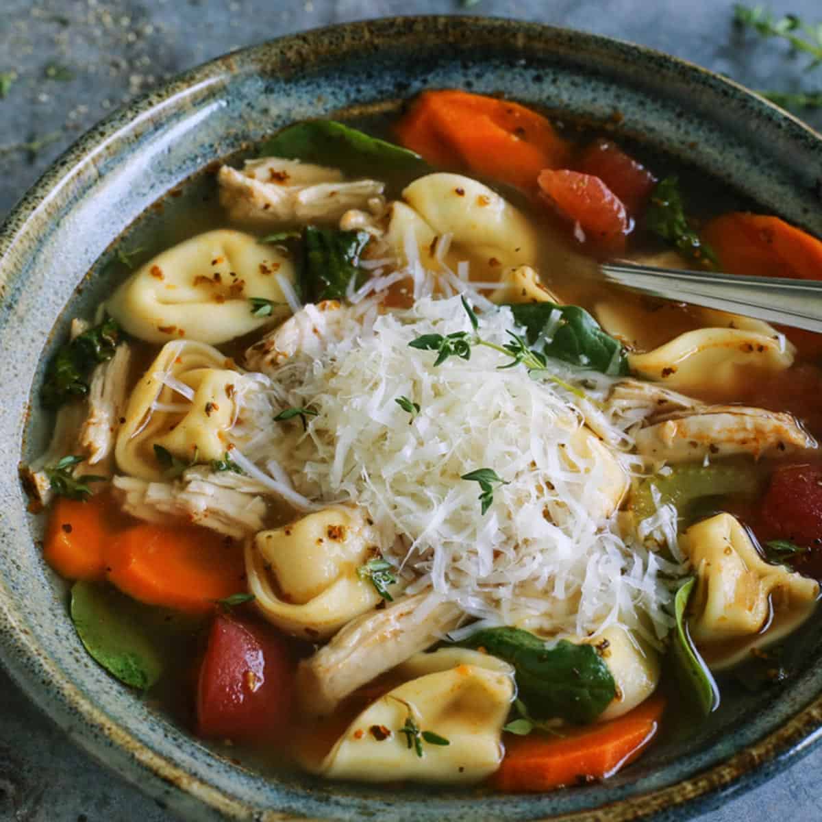 turkey tortellini soup in blue pottery bowl, with fresh Parmesan and herbs