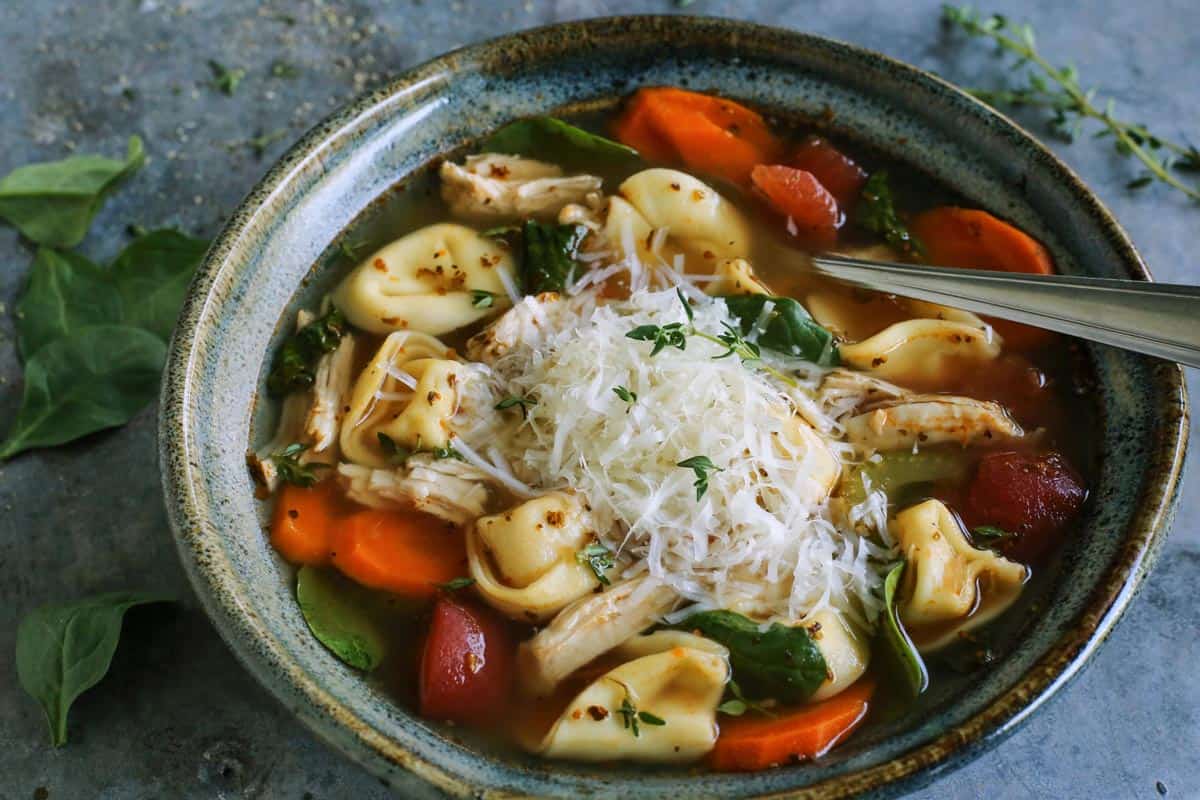 turkey tortellini soup in blue pottery bowl, with fresh Parmesan and herbs