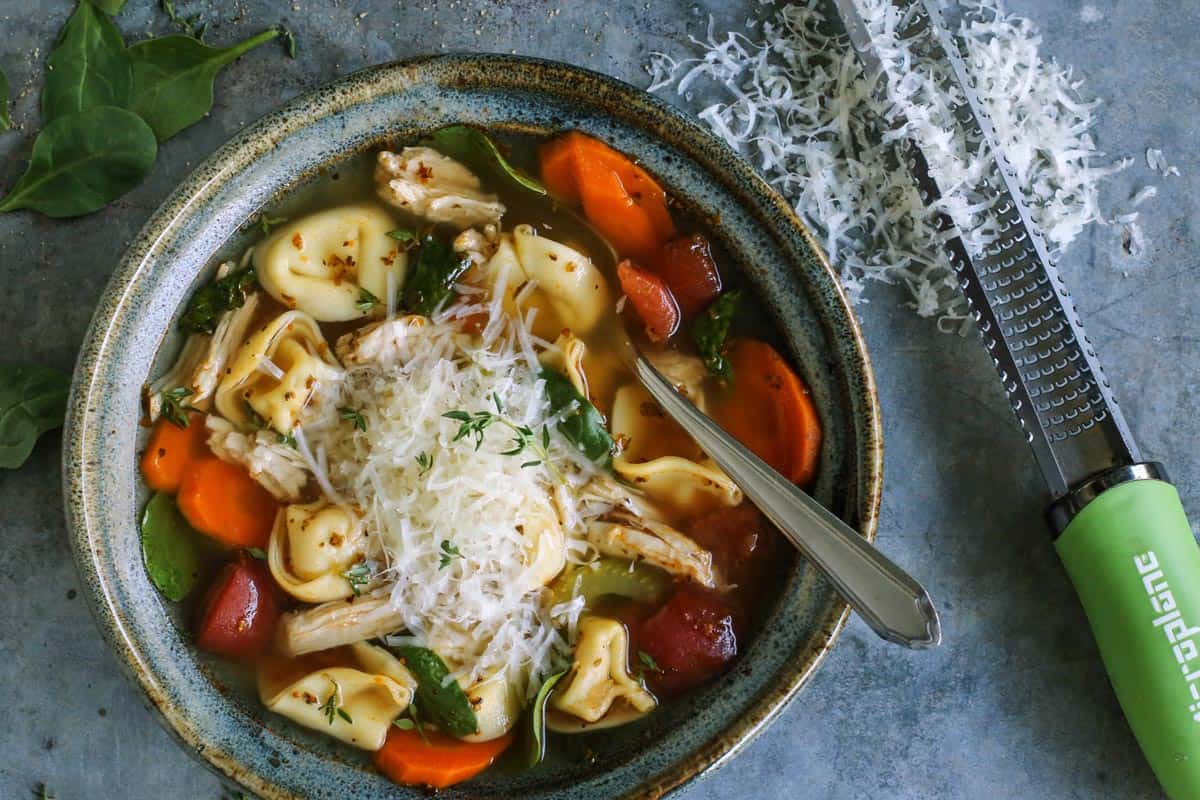 turkey tortellini soup in blue pottery bowl, with freshly grated Parmesan