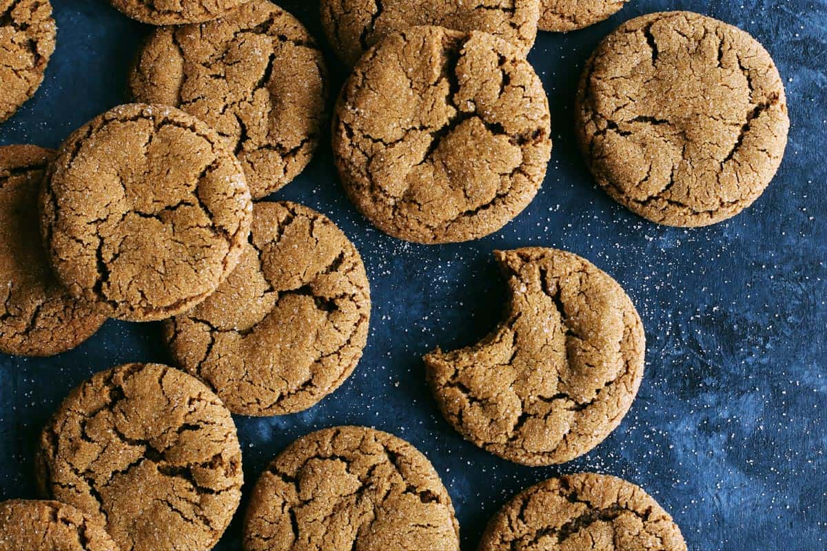 a batch of ginger cookies on a dark blue background, one cookie has a big bite out of it
