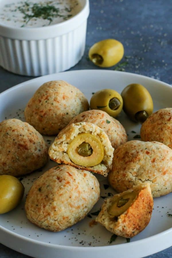 baked olive jalapeno cheese balls on a plate - with a cup of buttermilk ranch dip on the side