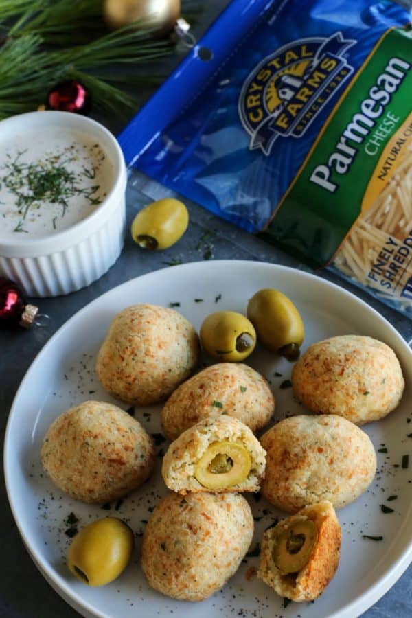 baked olive jalapeno cheese balls on a plate - with a package of Crystal Farms Parmesan cheese and a cup of buttermilk ranch dip on the side