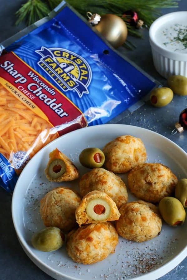 baked olive cheese balls on a plate - with a cup of buttermilk ranch dip and package of Crystal Farms Sharp Cheddar cheese on the side