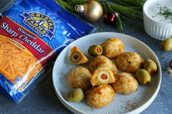 baked olive cheese balls on a plate - with a cup of buttermilk ranch dip and package of Crystal Farms Sharp Cheddar cheese on the side