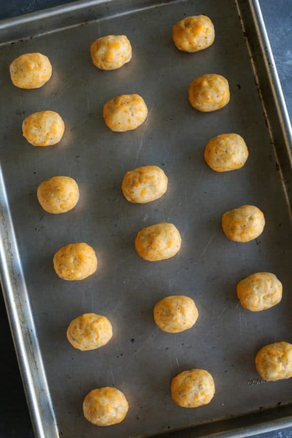 olives wrapped in cheese dough, lined up on a rimmed baking pan