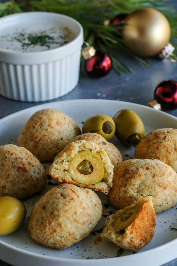 baked olive jalapeno cheese balls on a plate and a cup of buttermilk ranch dip on the side