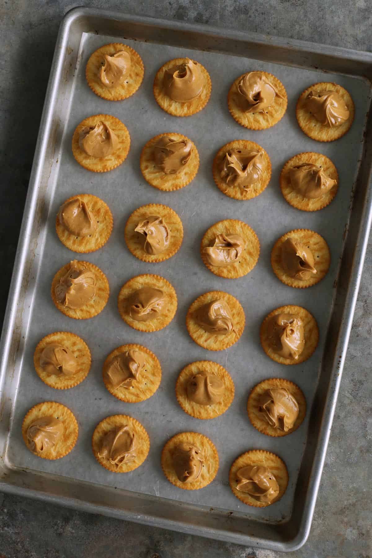 Ritz crackers with peanut butter on them, lined up on a rimmed pan