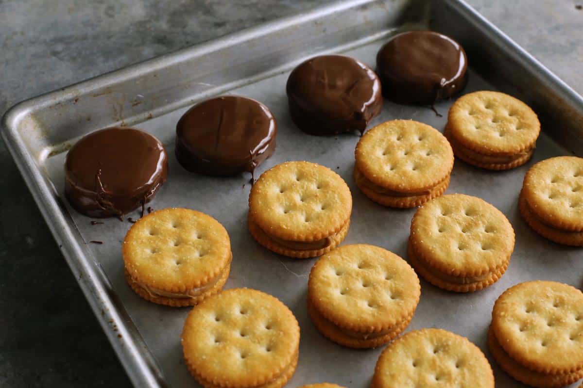 Ritz sandwich crackers with peanut butter inside, some are dipped in chocolate, lined up on a rimmed pan