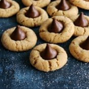 pinterest image of peanut butter blossoms cookies with a Hershey's Kiss laid out on a dark blue countertop