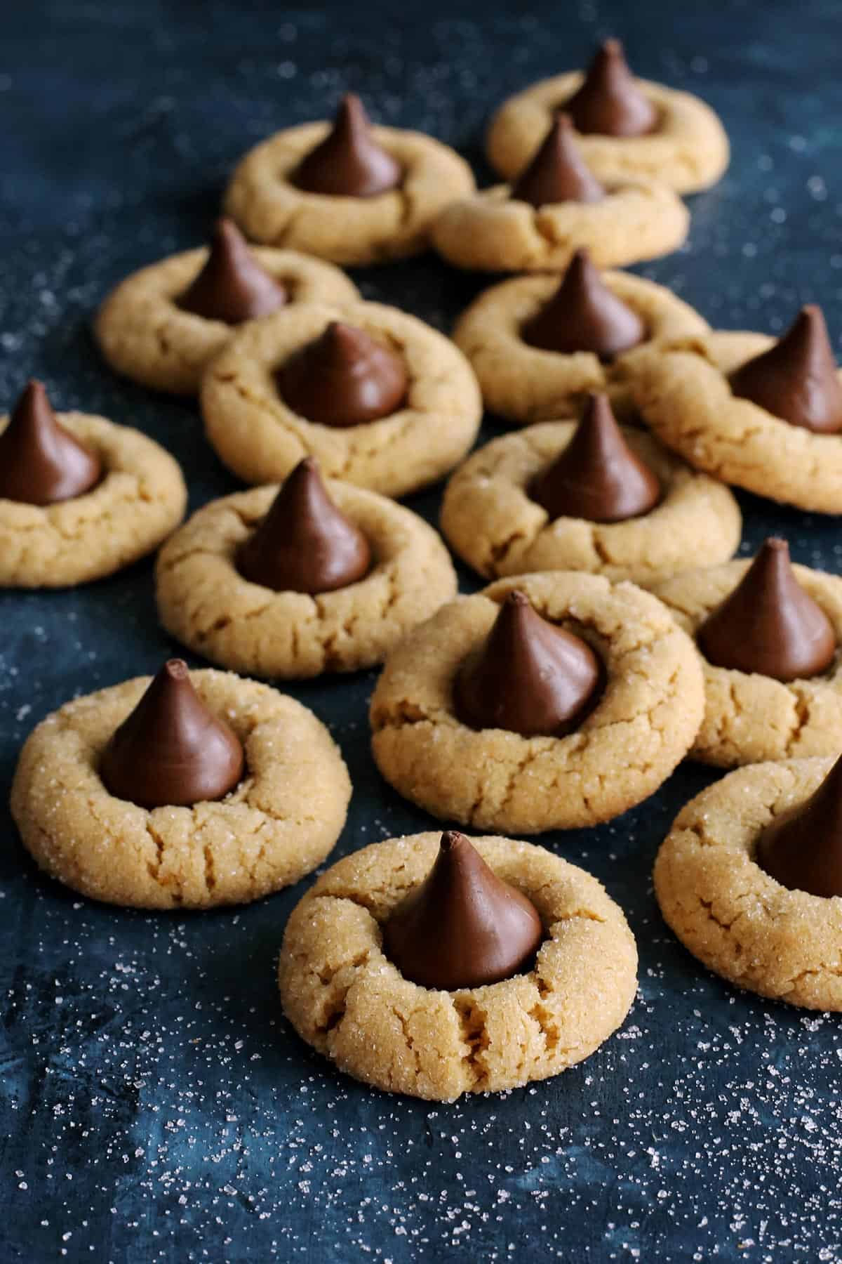 Peanut Butter Blossoms are soft & chewy cookies with a crackly sugar crust and chocolate kiss in the center. An easy Christmas cookie recipe! a pile of peanut butter cookies with chocolate kisses