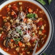 meatball soup in a white bowl, with fresh basil