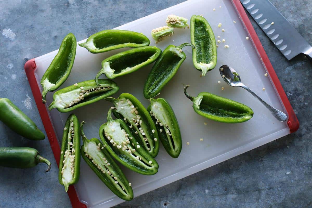 Jalapeno peppers sliced in half, sitting on a cutting board