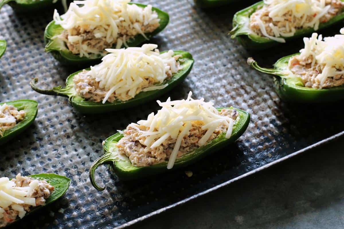 roasted jalapeno halves on a pan, stuffed with Italian sausage, sprinkled with shredded mozzarella cheese