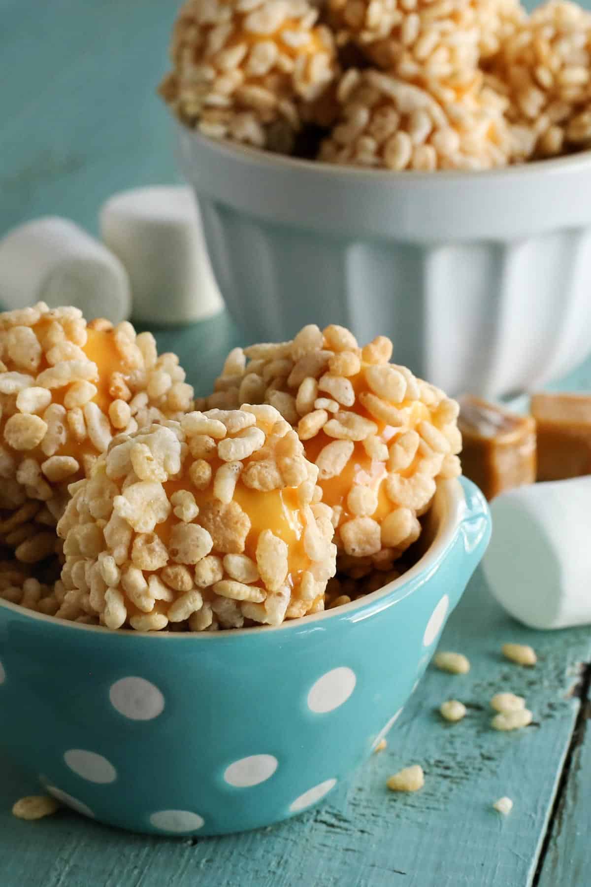big marshmallows coated in caramel and Rice Krispies cereal, in a turquoise dotted bowl