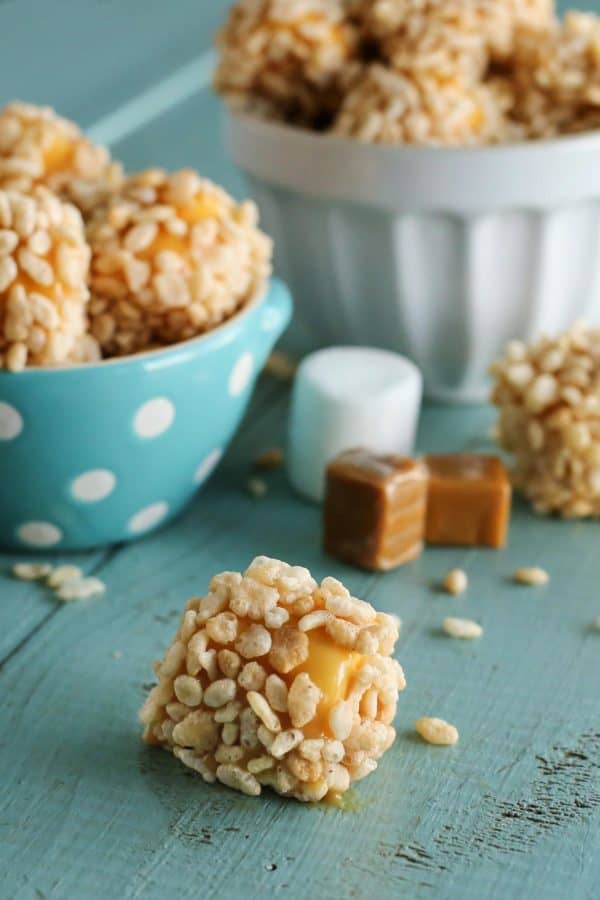 a marshmallow coated with caramel and rice krispies with a bowl of marshmallows in the background