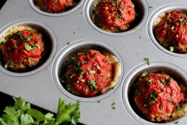 Mini Italian meatloaves in a muffin tin with cheese oozing out of them