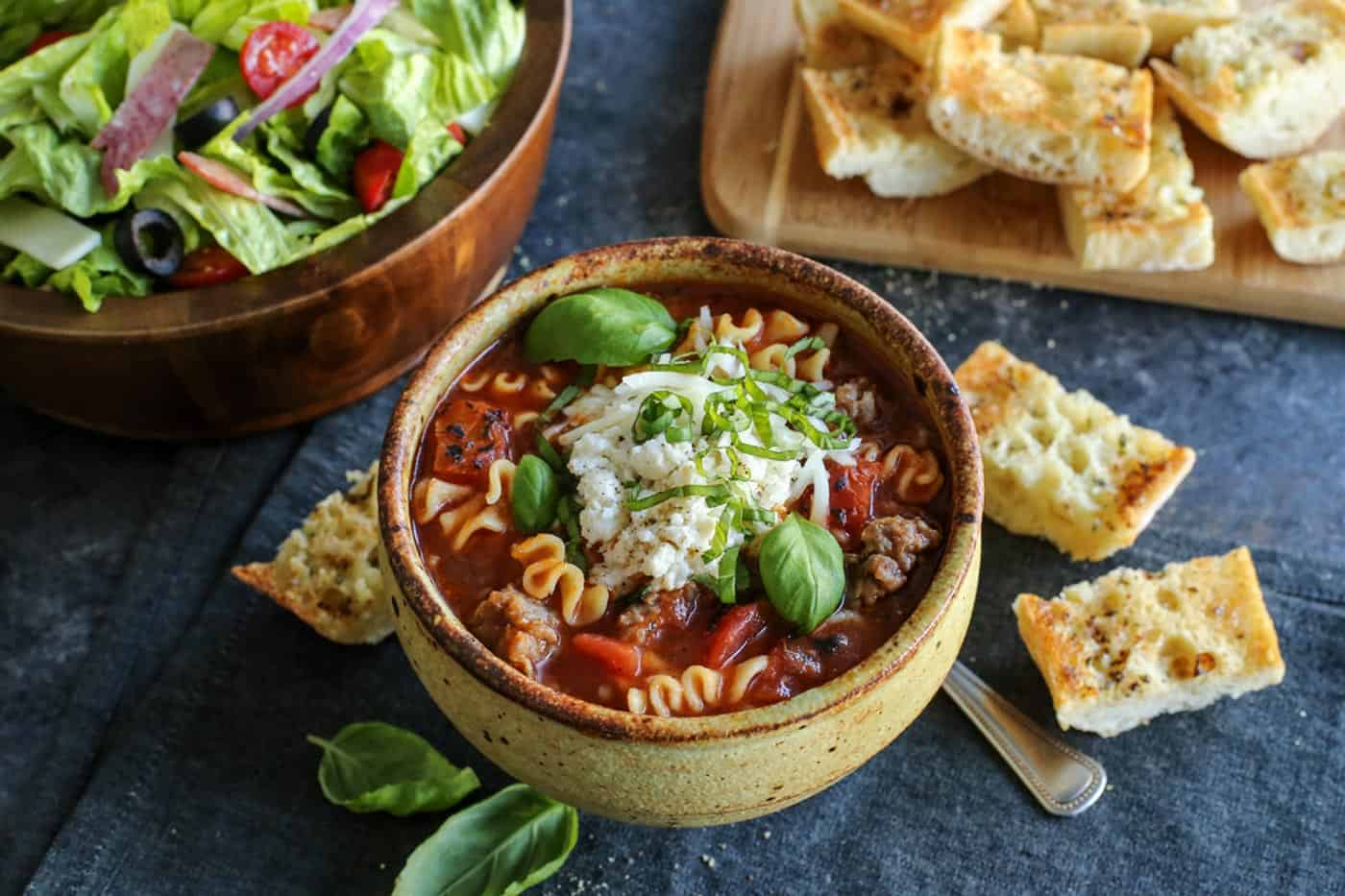 a bowl of soup, bowl of salad, pieces of garlic toast