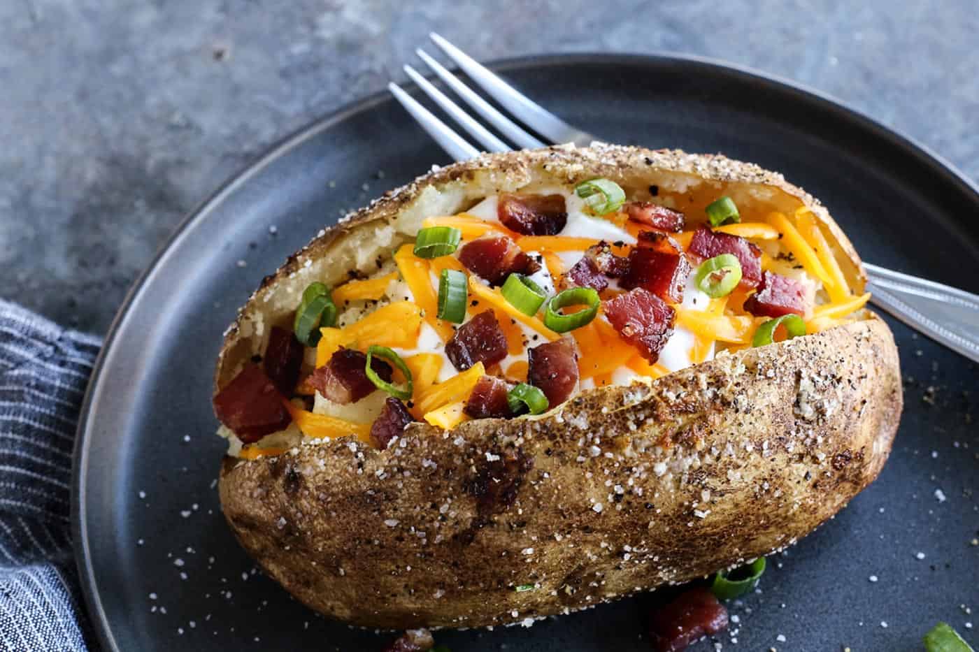 baked potato on a plate, topped with cheese and bacon