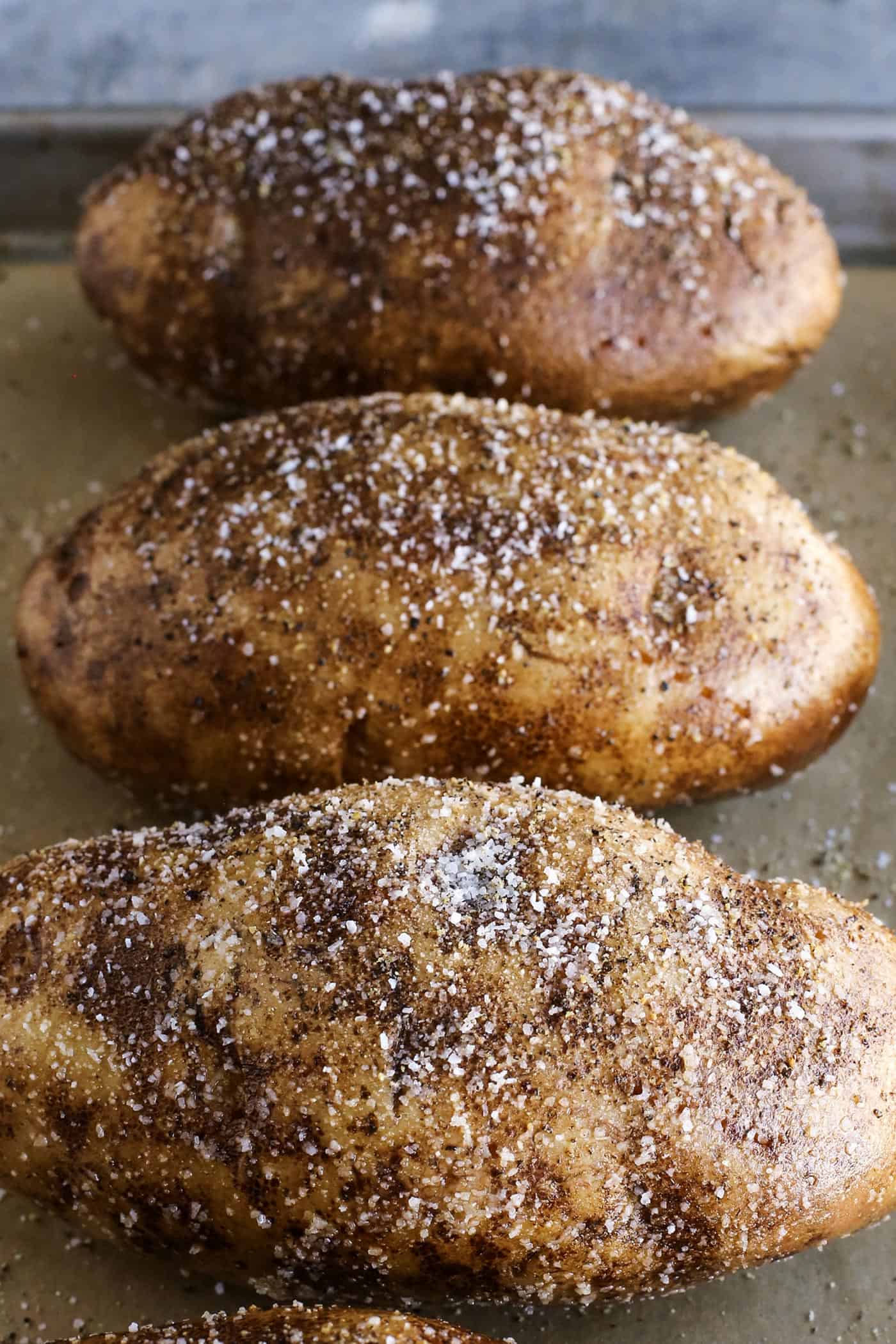 large potatoes on a baking pan, with olive oil, salt, pepper, and garlic powder
