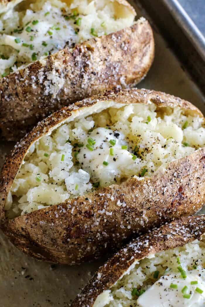 baked potatoes on pan, split open, with butter and chives