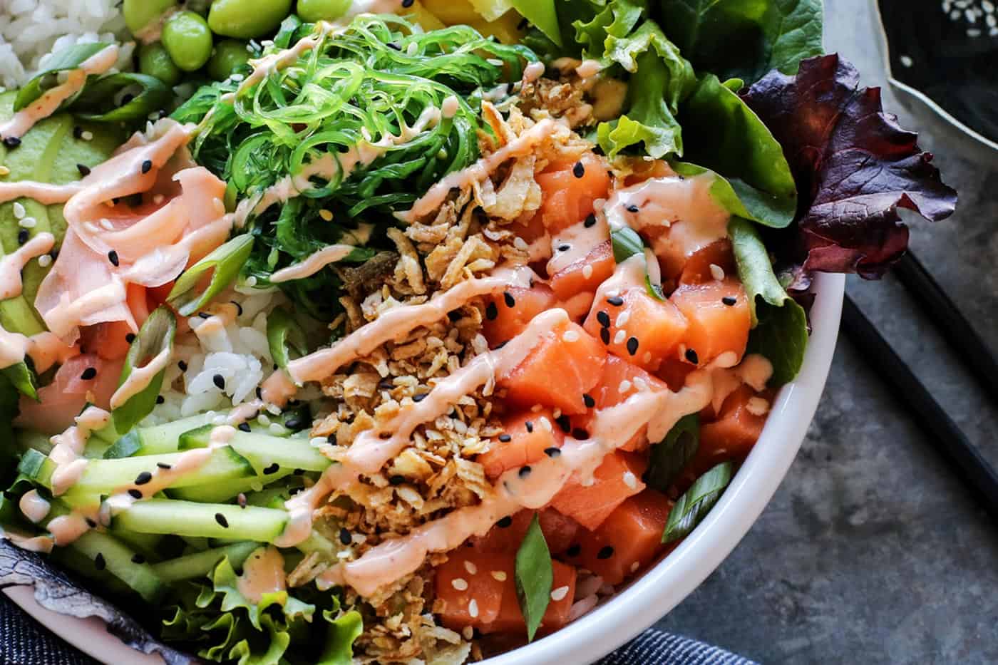 A white bowl filled with diced sushi grade fish, greens, rice and other poke ingredients