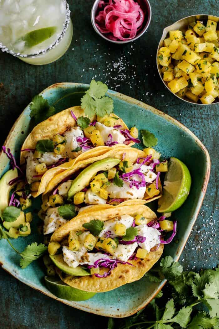fish tacos with roasted pineapple on a plate, plus pickled red onions and a margarita 