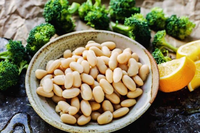 great northern beans in a bowl, broccoli florets, and fresh lemon wedges