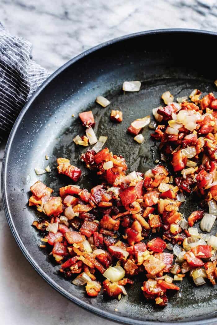 a skillet with pieces of fried bacon and shallots