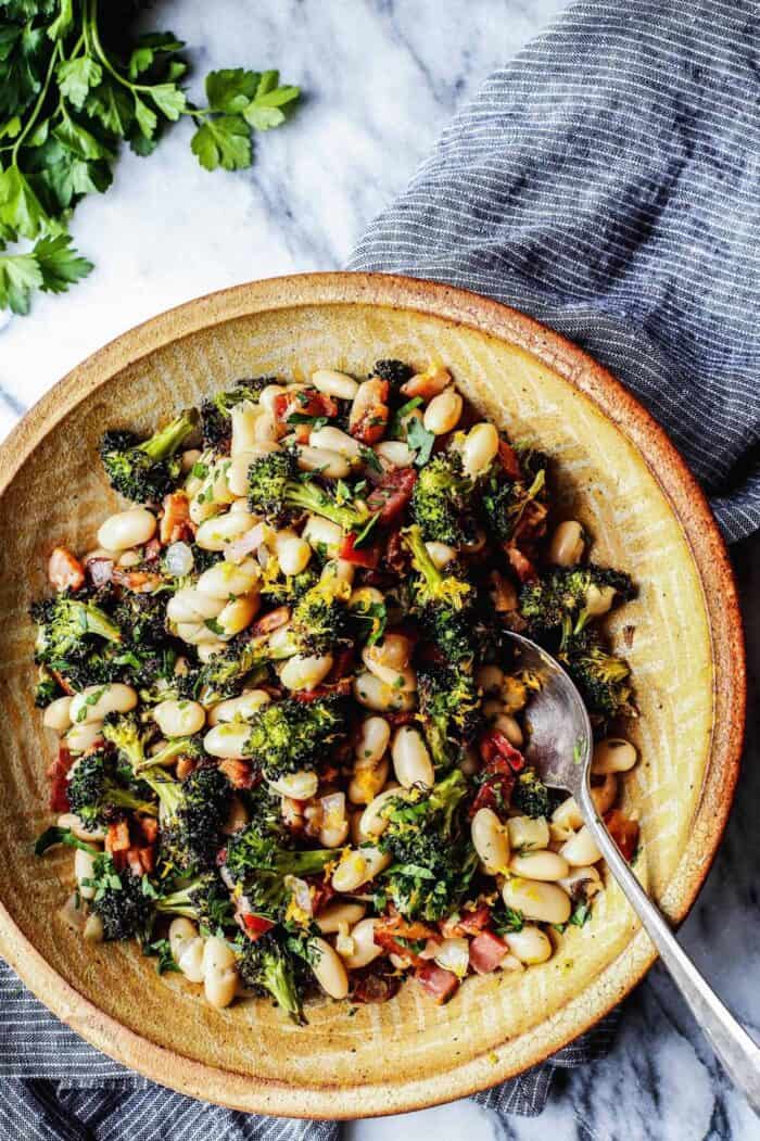 white beans, roasted broccoli, bacon bites, and fresh lemon in a pottery bowl