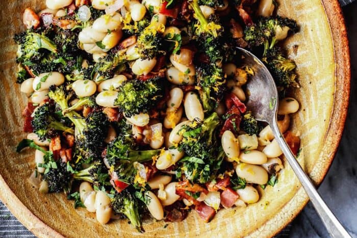 a pottery bowl with great northern beans, roasted broccoli, fried bacon, and lemon 