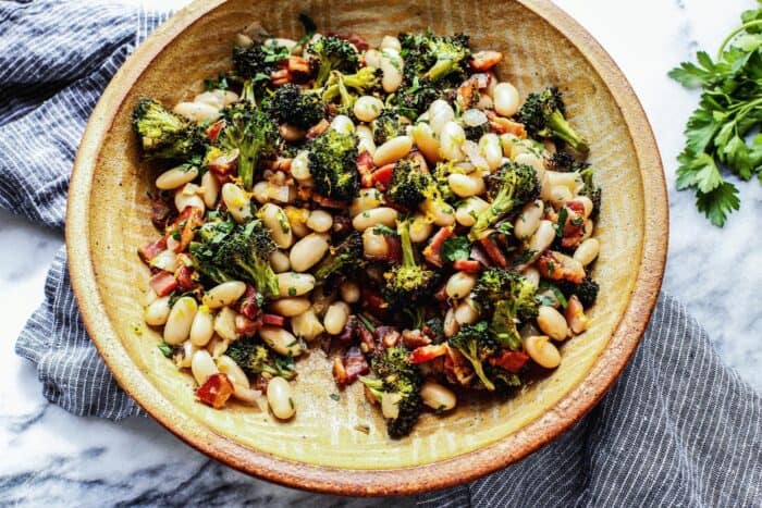 a pottery bowl with white beans, roasted broccoli, fried bacon, and lemon 