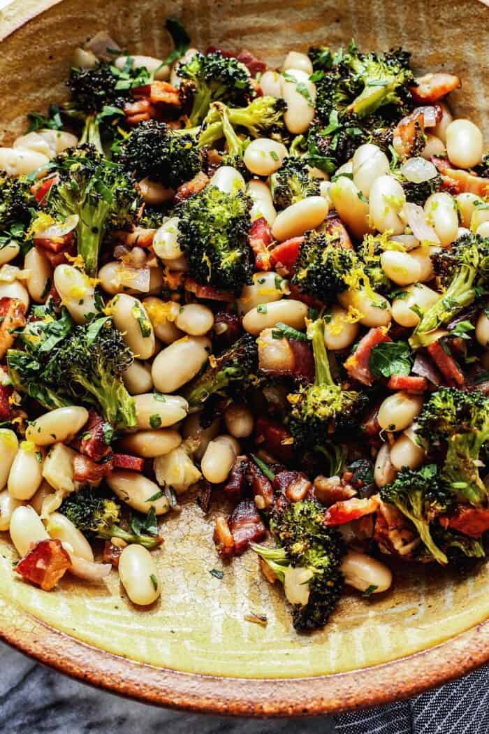 a pottery bowl with white beans, roasted broccoli, fried bacon, and lemon 