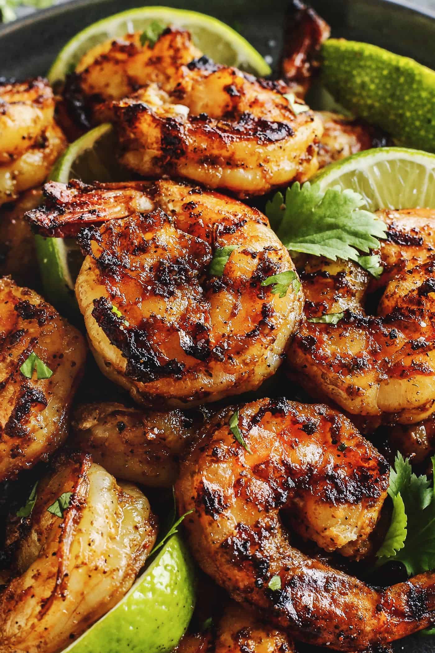 Grilled shrimp with limes, piled on a black plate.