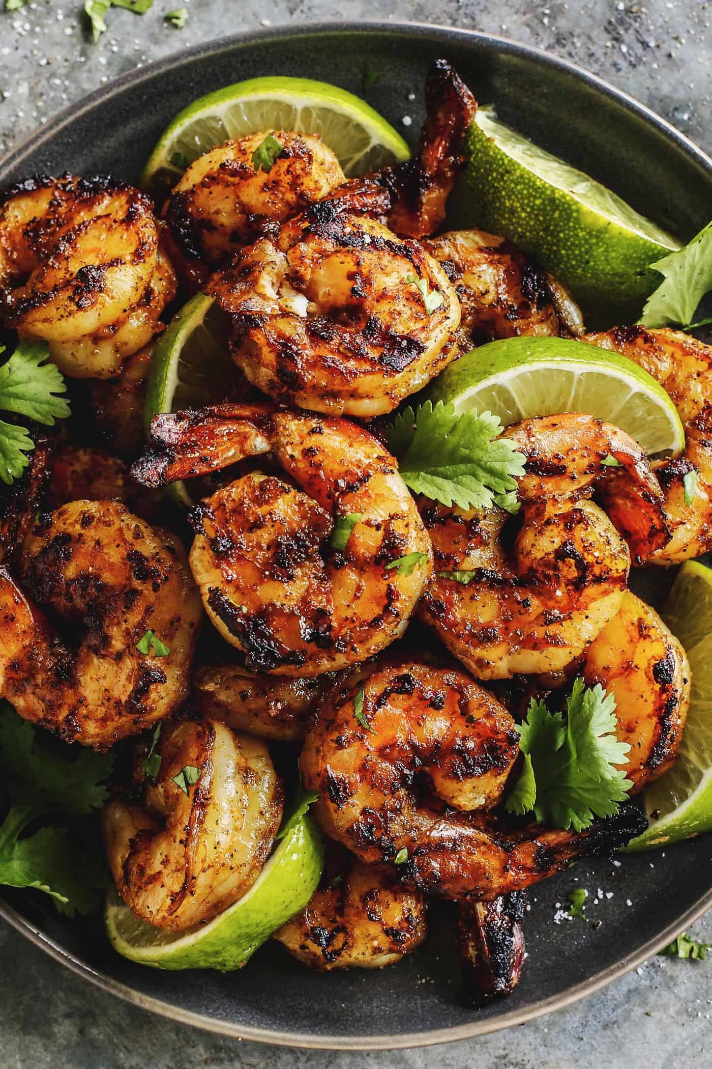 Margarita grilled shrimp and limes on a black plate.