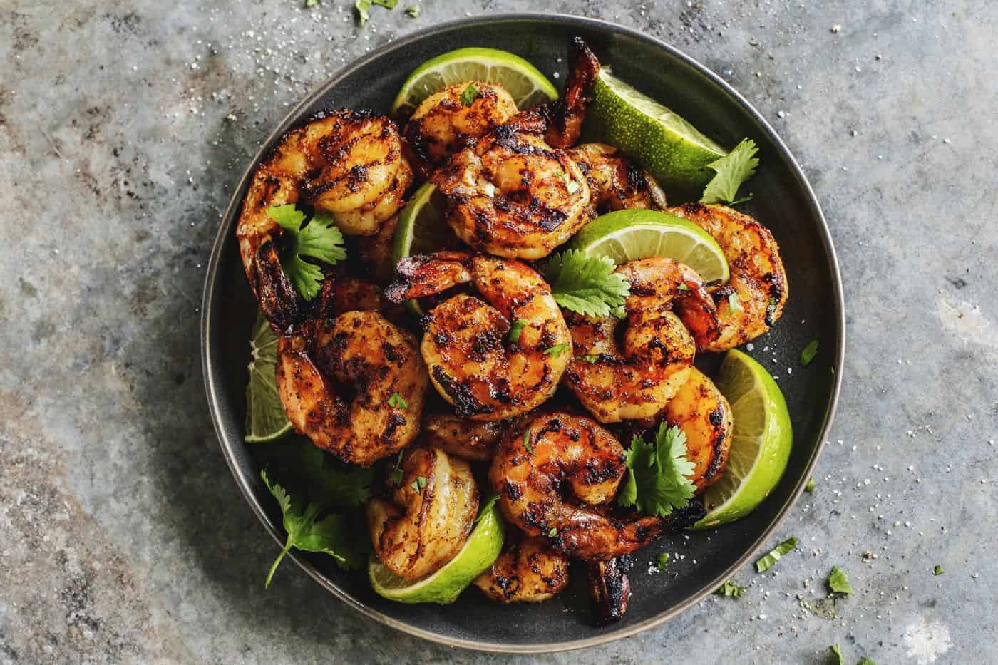 Grilled shrimp and limes on a black plate.