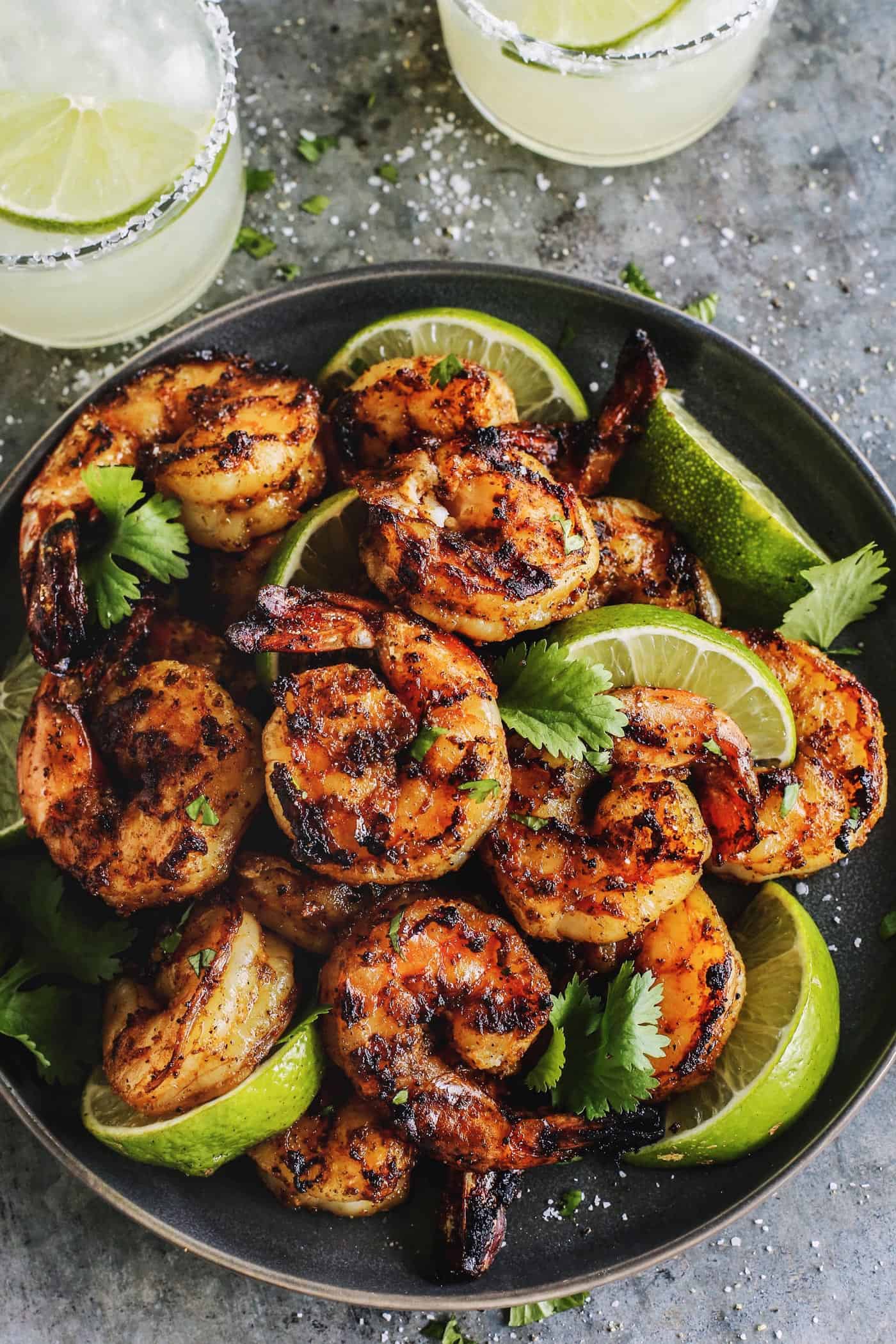 grilled shrimp and lime wedges on black plate, plus two margaritas