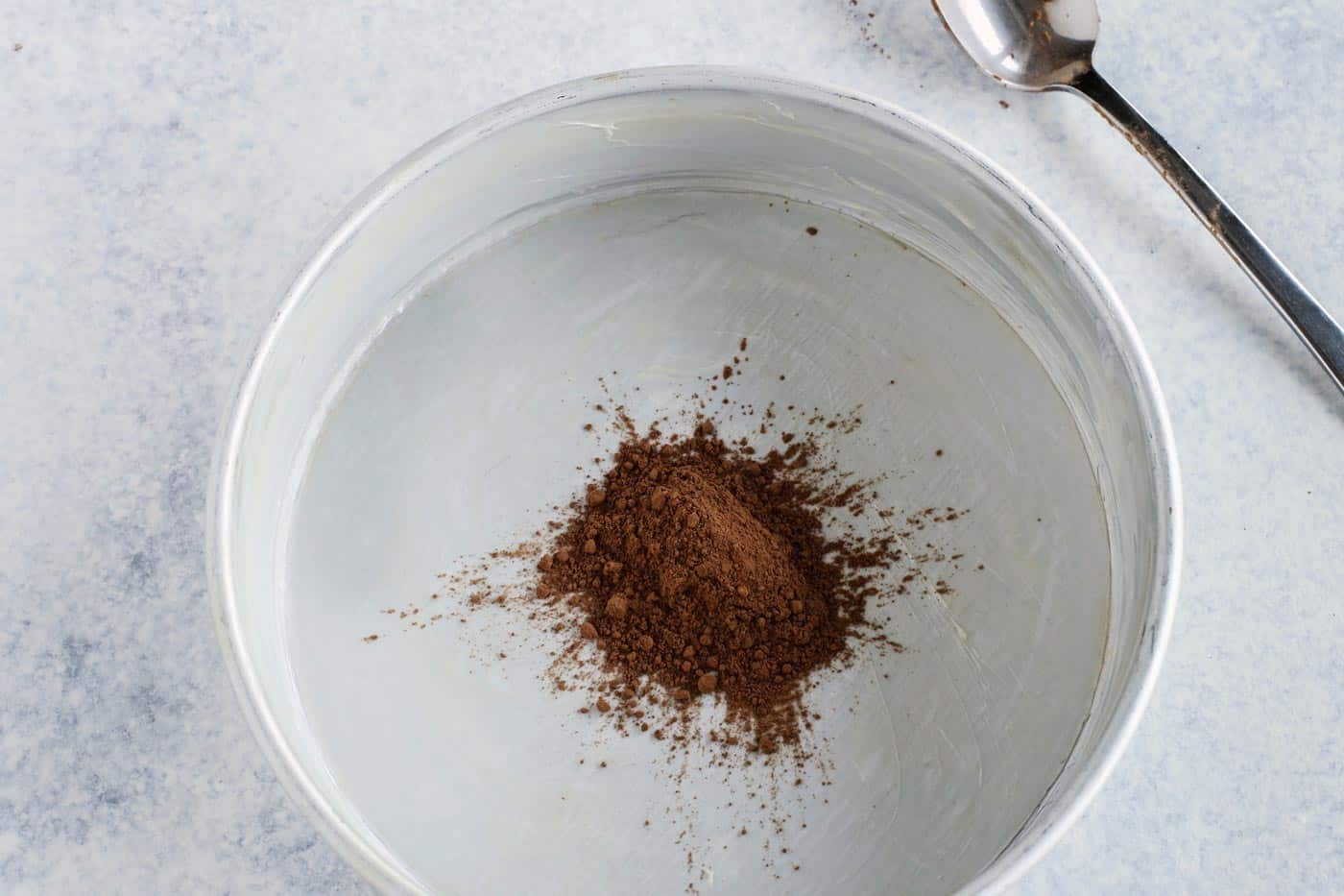 a round cake pan that has been buttered and lined with a piece of parchment paper, with cocoa powder in the center for dusting the pan