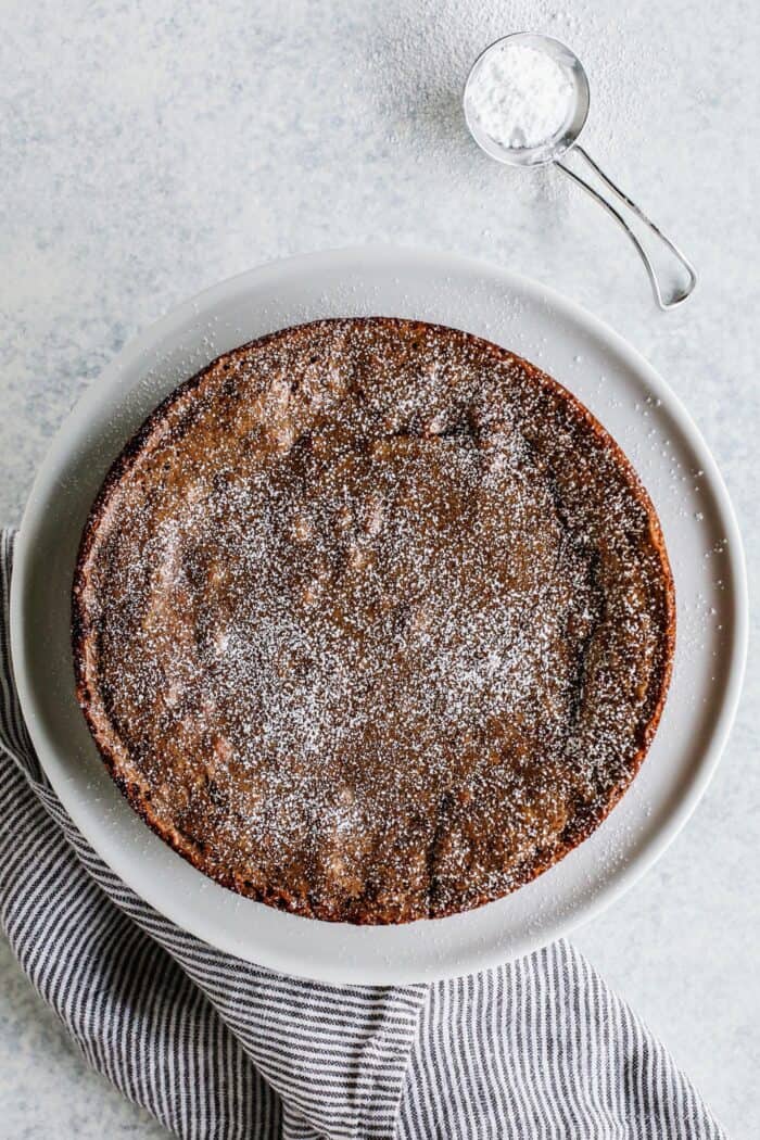 Kladdkaka cake dusted with powdered sugar, on a white cake plate