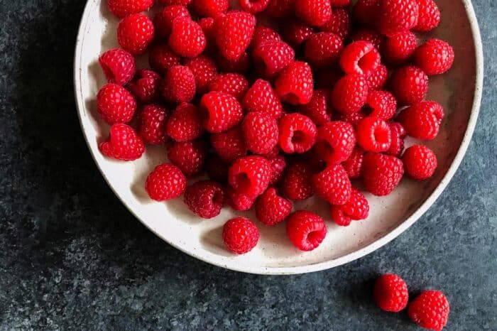 A low white pottery bowl filled with fresh raspberries