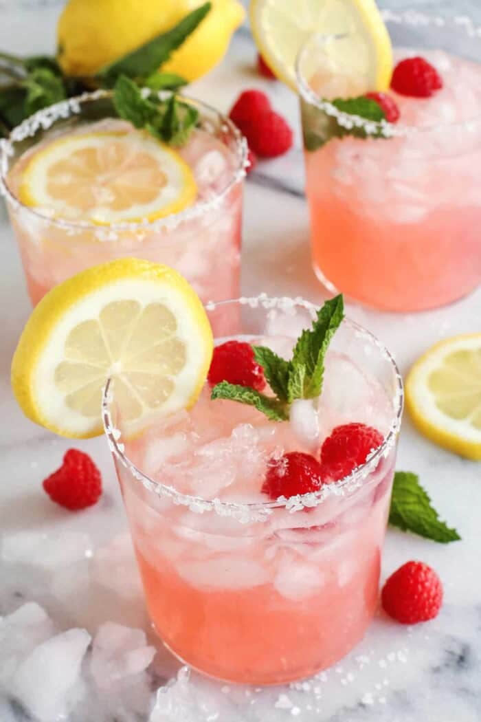 three glasses of pink lemonade margarita with fresh lemon, raspberries, and mint