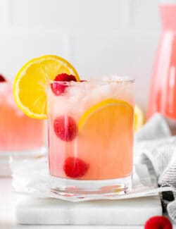 A pink lemonade margarita garnished with raspberries and lemon