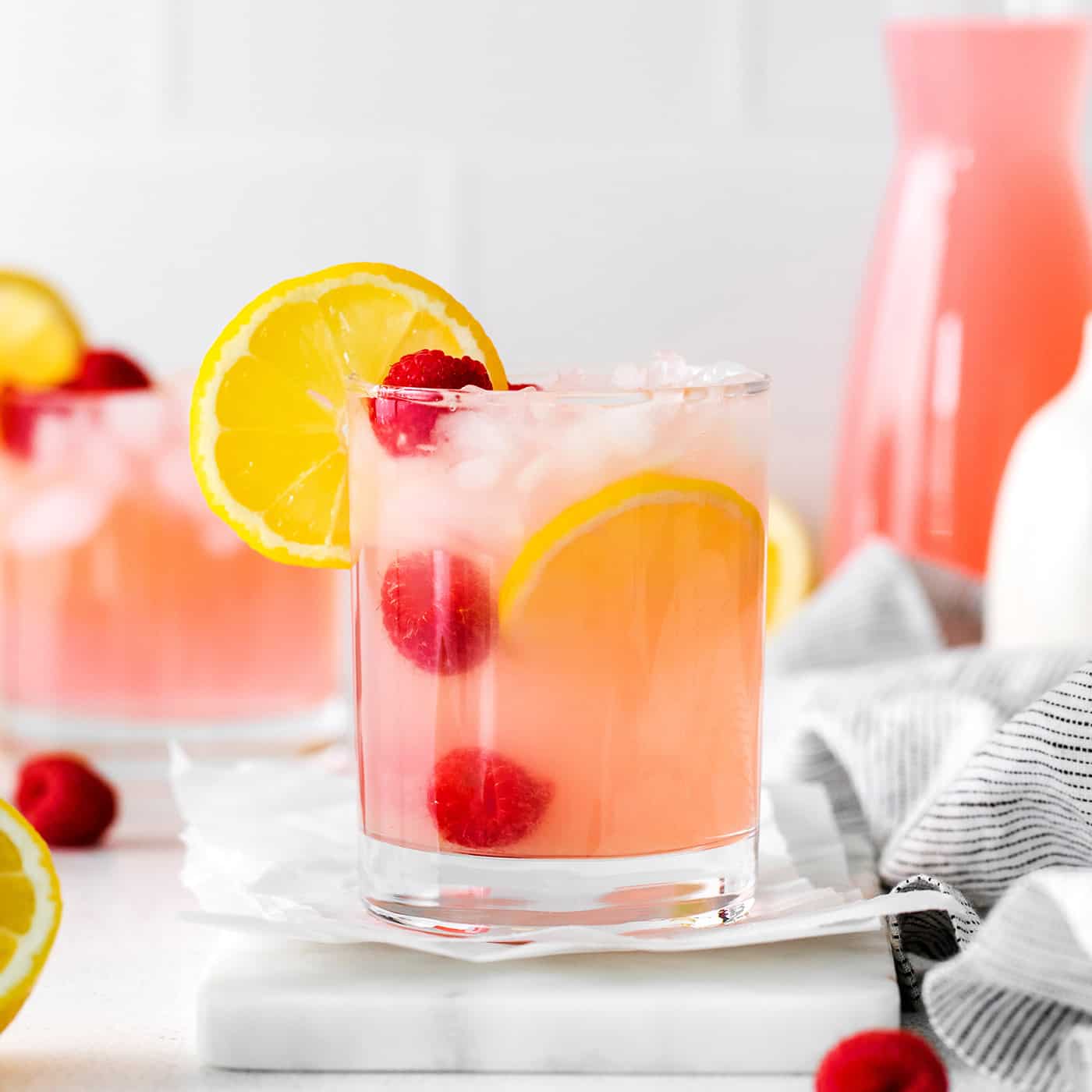 A pink lemonade margarita garnished with raspberries and lemon
