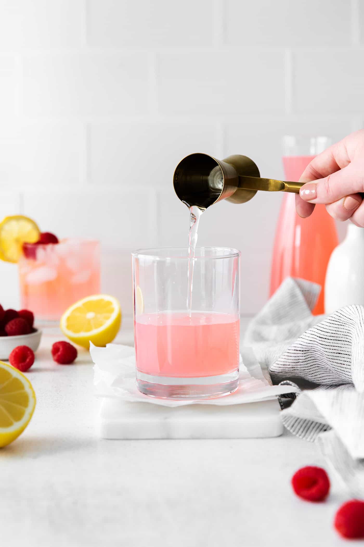 Tequila being added to a glass with pink lemonade